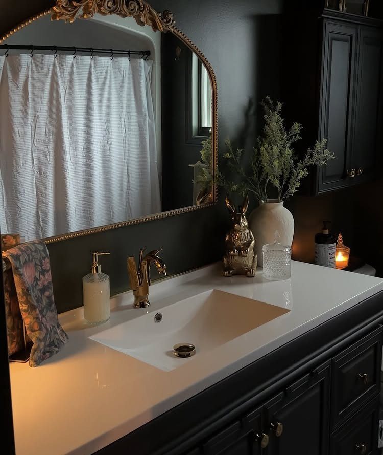 Bathroom vanity with gold mirror reflecting a white shower curtain and black rod
