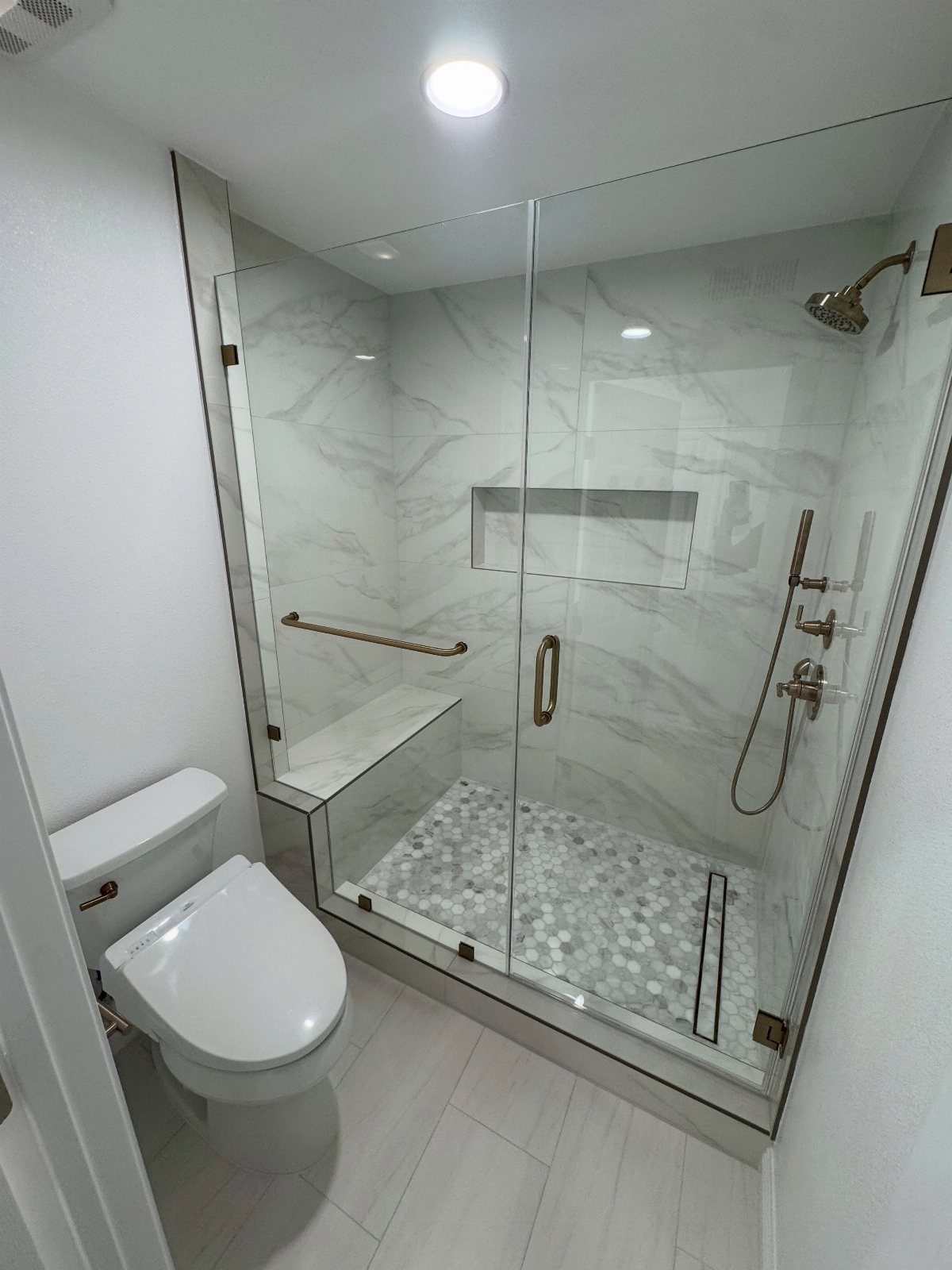 Modern bathroom shower with white marble wall tiles and pebble stone flooring.