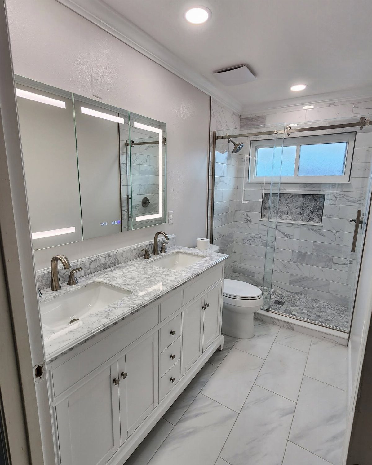Modern bathroom with white marble tile shower, double vanity, and white tiled flooring.