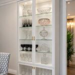 White wooden hutch with glass doors displaying crystal glassware in a dining room.