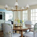 Light blue fabric dining chairs around a round wooden table under a gold chandelier.