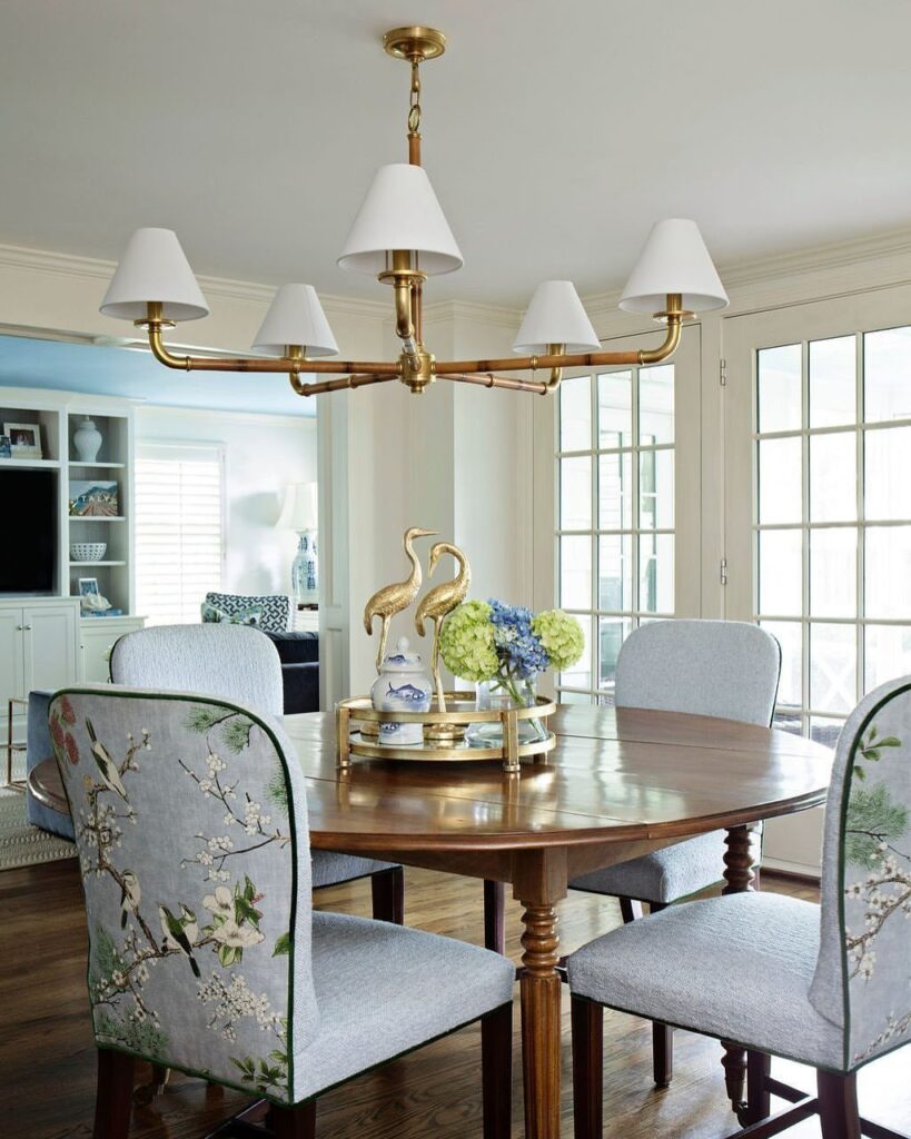 Light blue fabric dining chairs around a round wooden table under a gold chandelier.