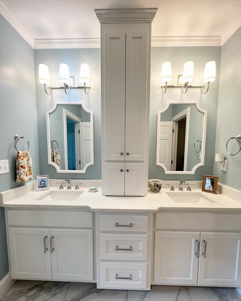 White double vanity bathroom featuring a tall central built-in storage cabinet and light blue walls.