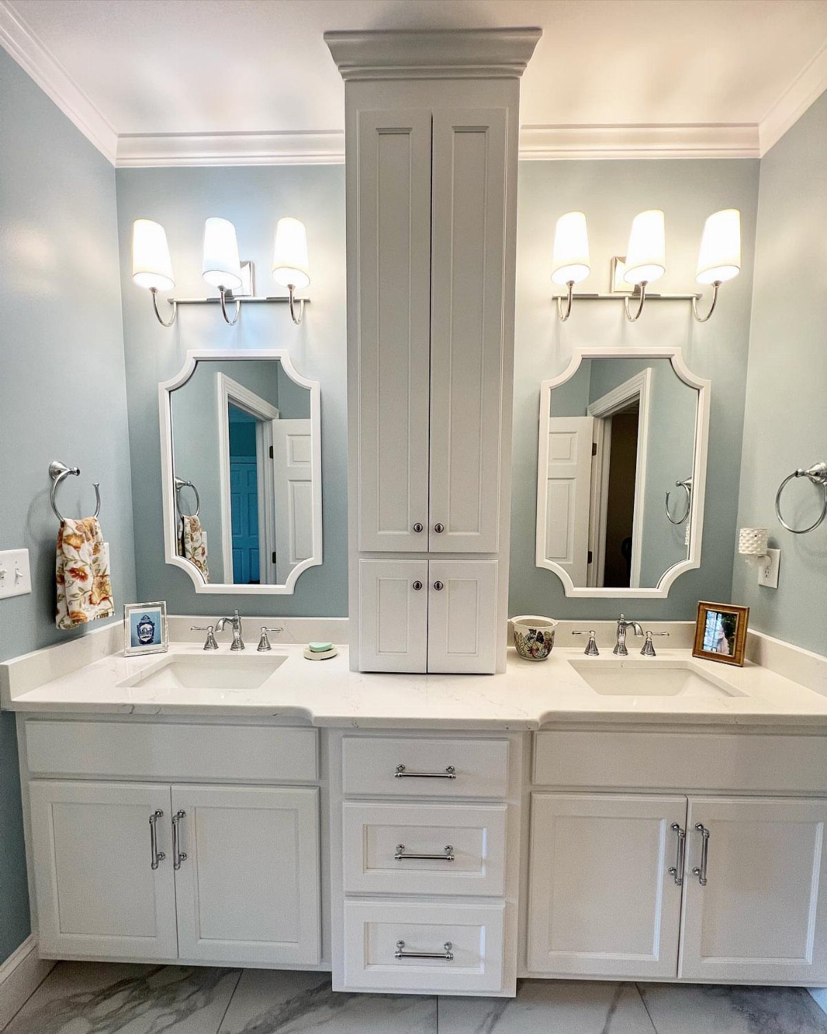 White double vanity bathroom featuring a tall central built-in storage cabinet and light blue walls.