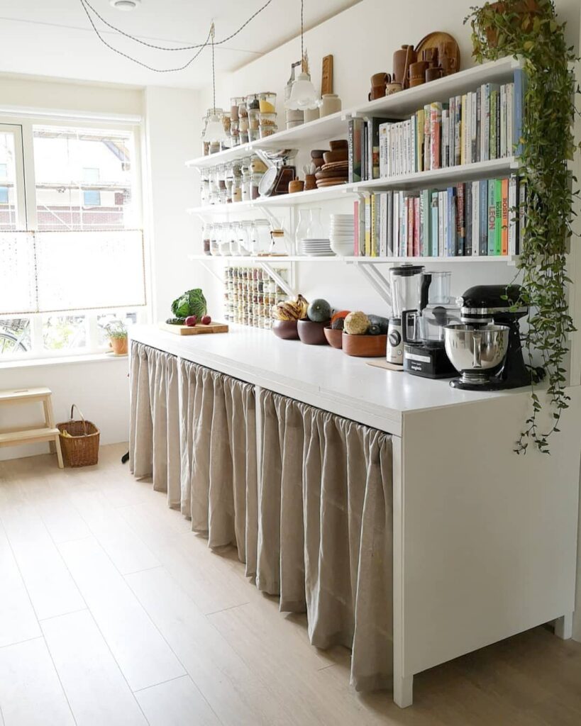 White open wall shelves with books and jars above a white kitchen counter.