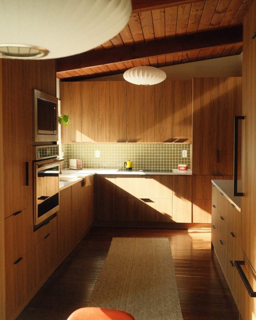 Mid century modern kitchen with wood cabinets, green tile backsplash, and saucer pendant lights.
