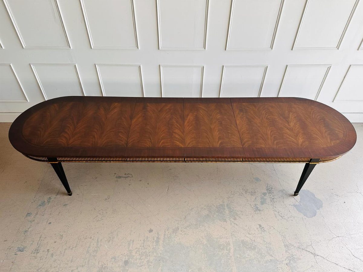 Oval mid century modern dining table with polished brown wood and tapered black legs.
