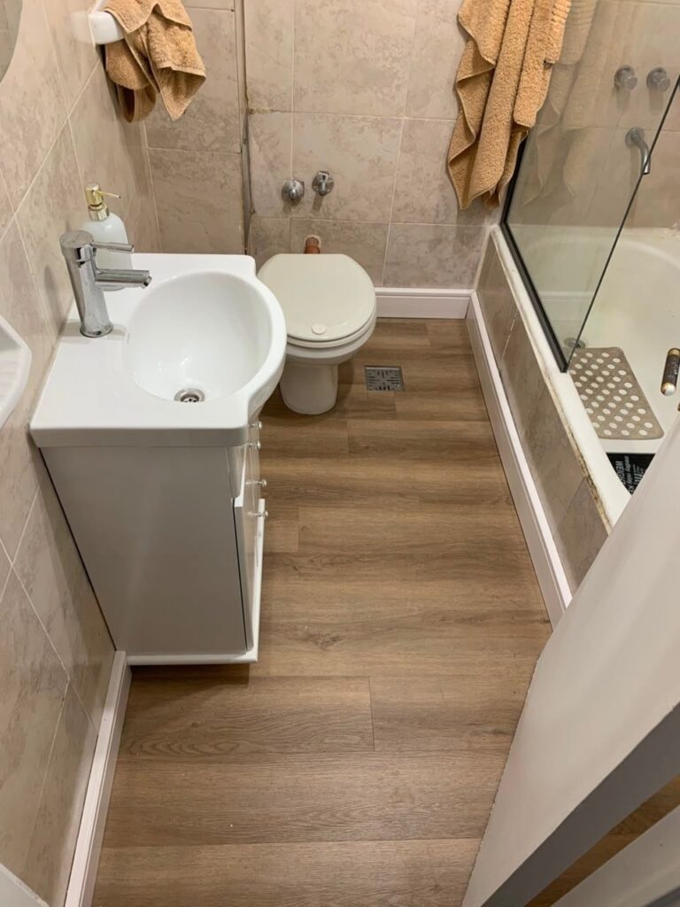 Brown wood-look vinyl plank flooring in a small bathroom with white fixtures.