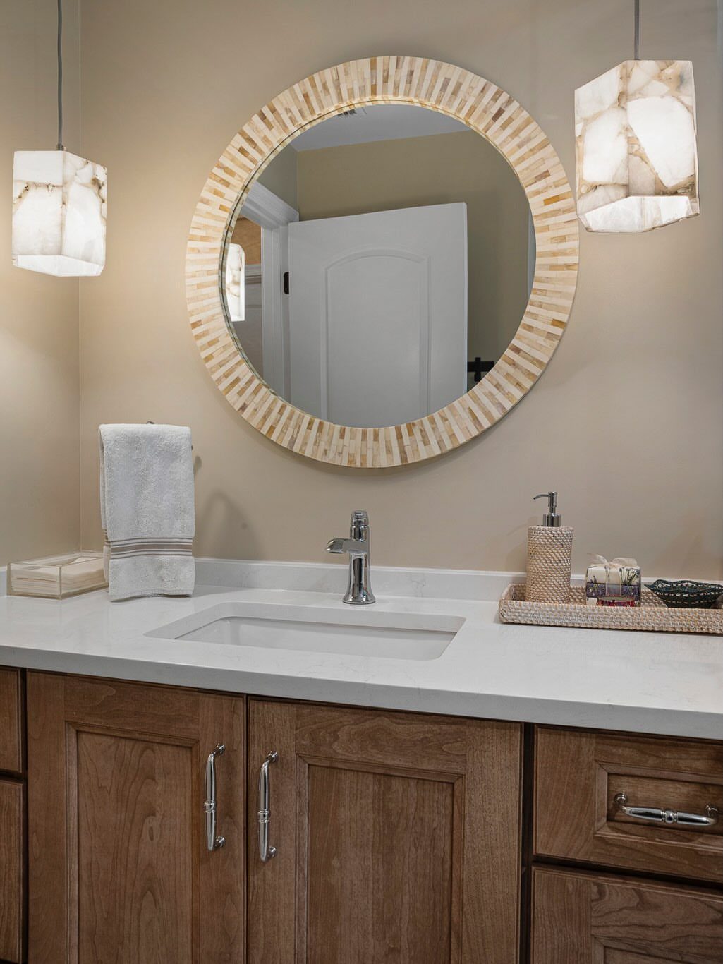Bathroom vanity with a round gold mirror and two modern square pendant lights.