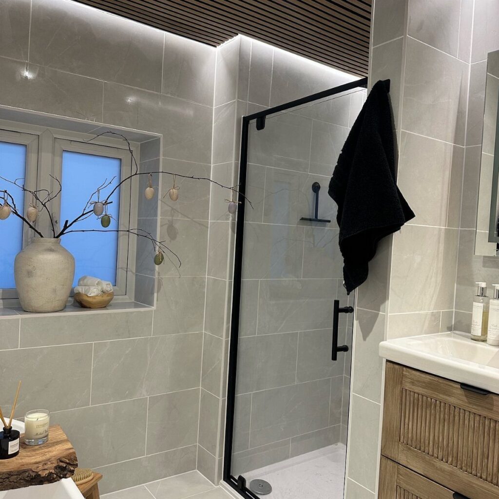Modern bathroom with grey tiles, black framed shower, and wooden vanity sink.