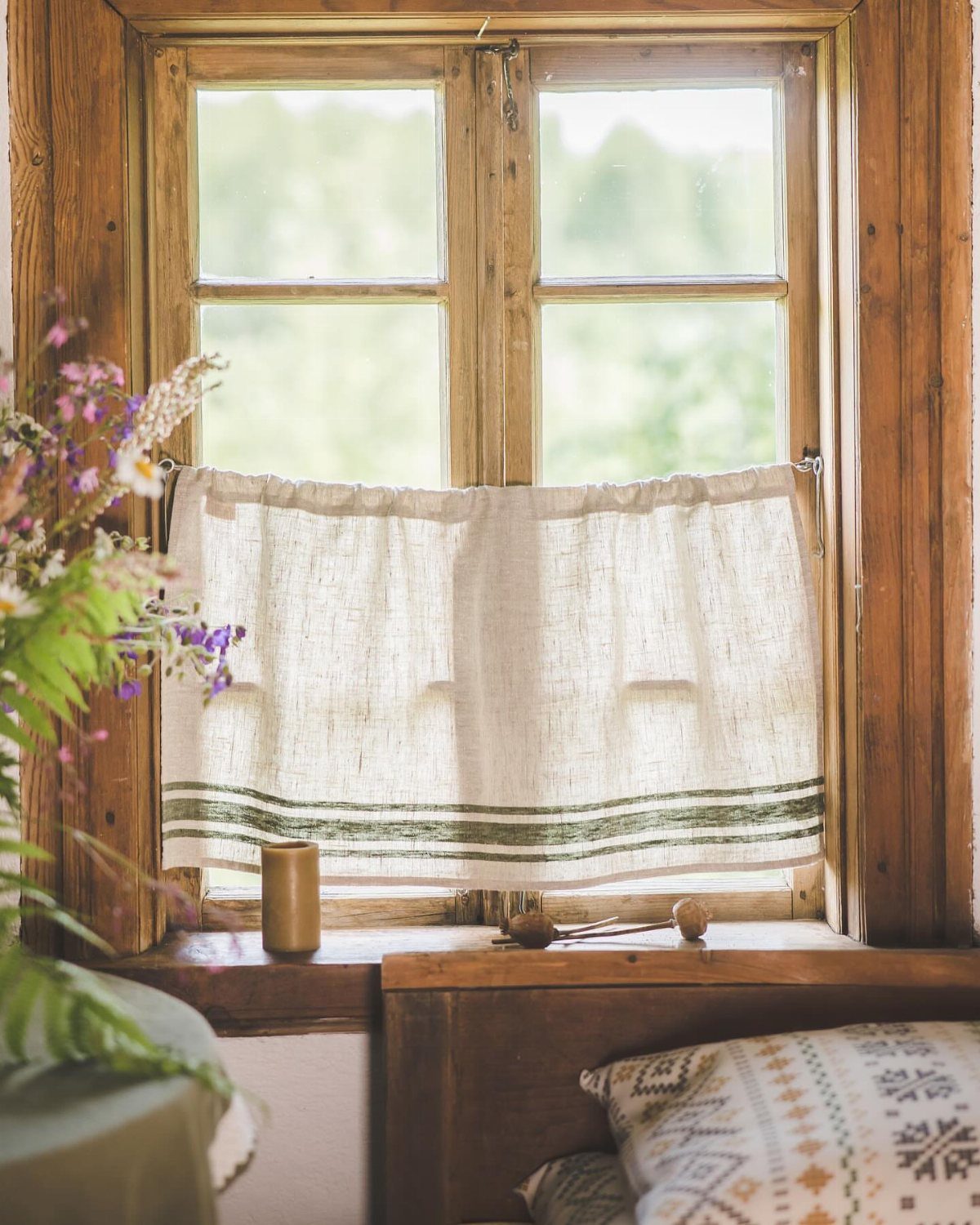 Short off-white linen cafe curtains with green stripes on a rustic wooden window.