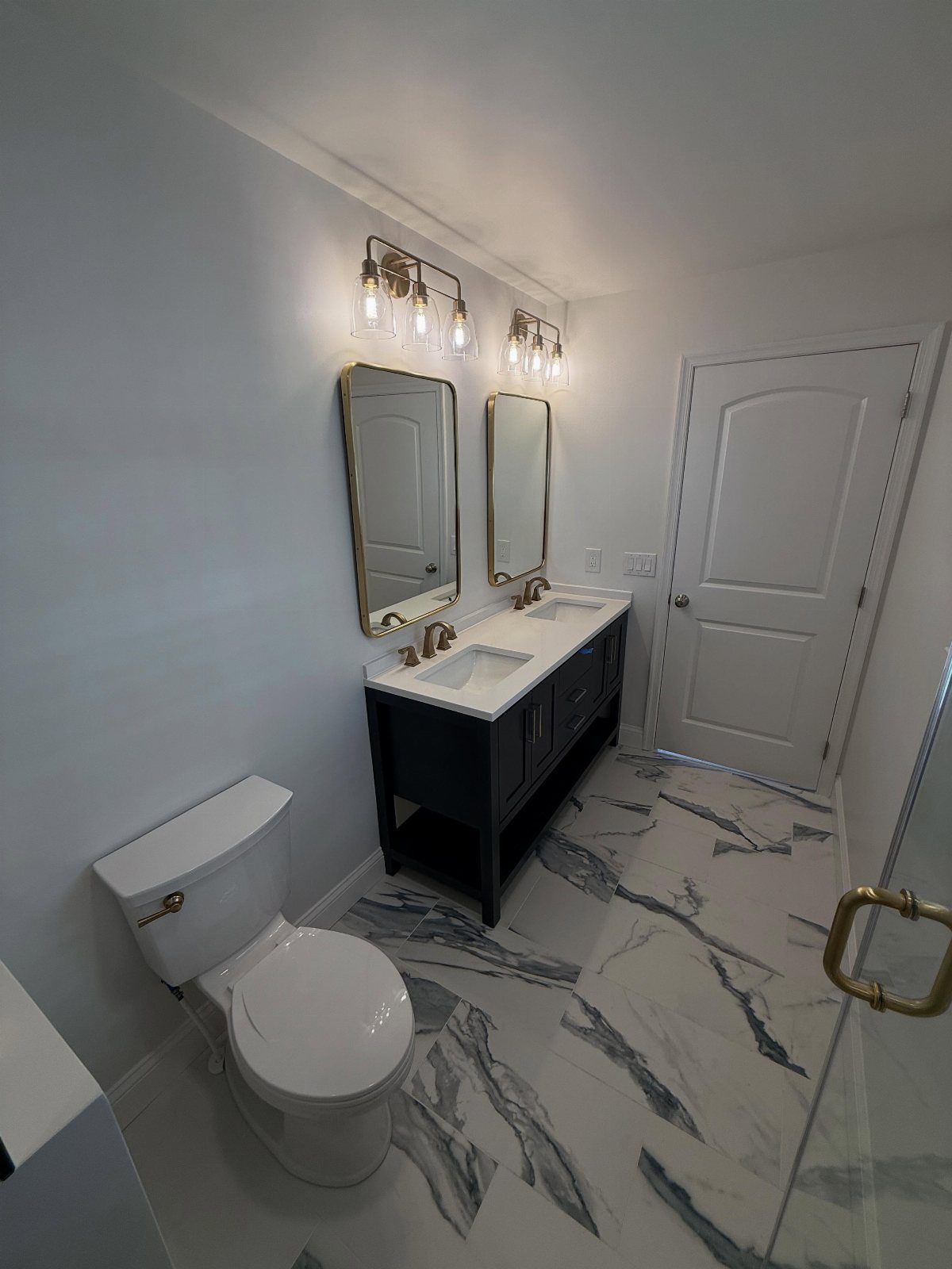 Small master bathroom with blue double vanity, gold accents, and marble floors.
