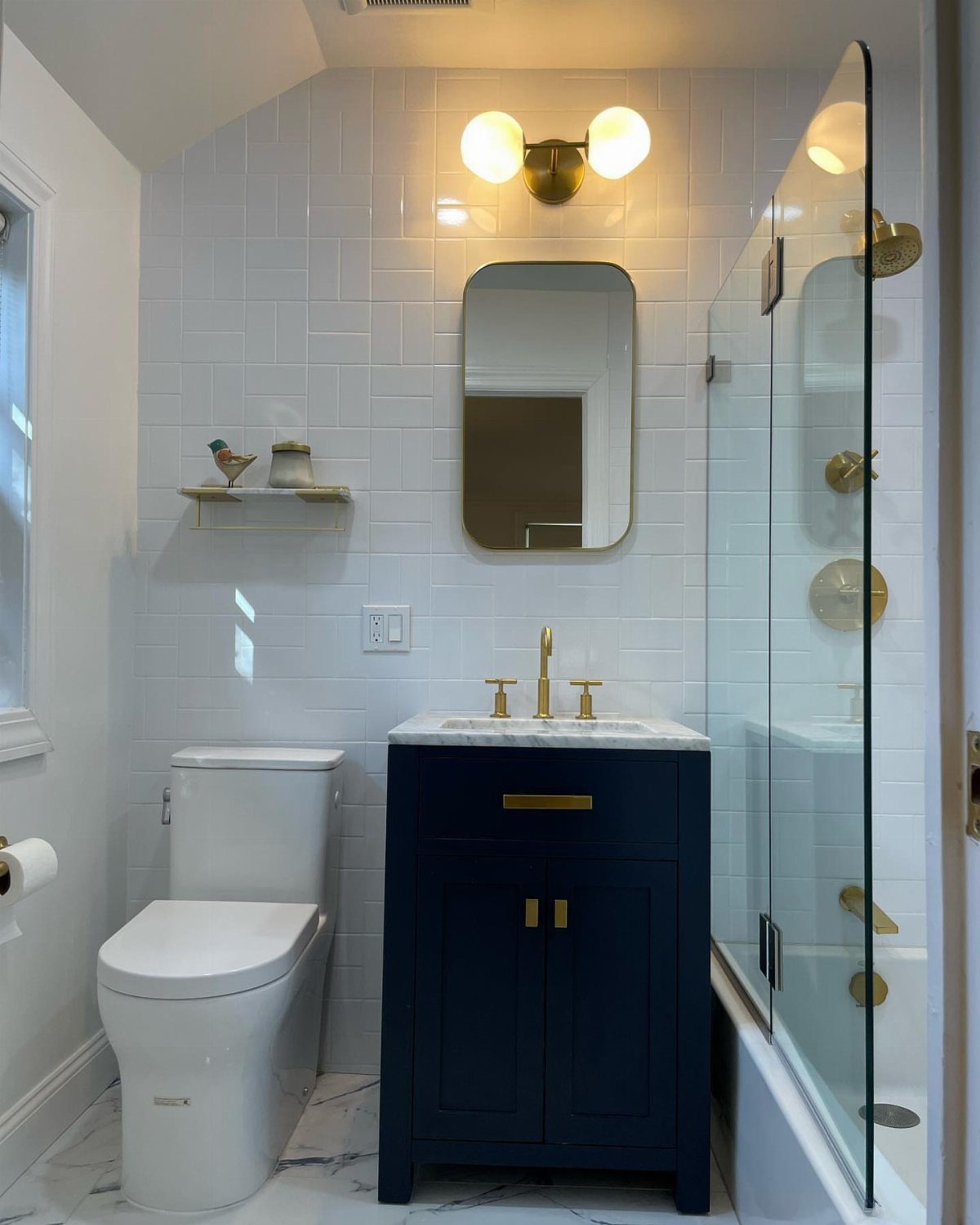 Navy blue vanity with marble top in a small white tiled bathroom.