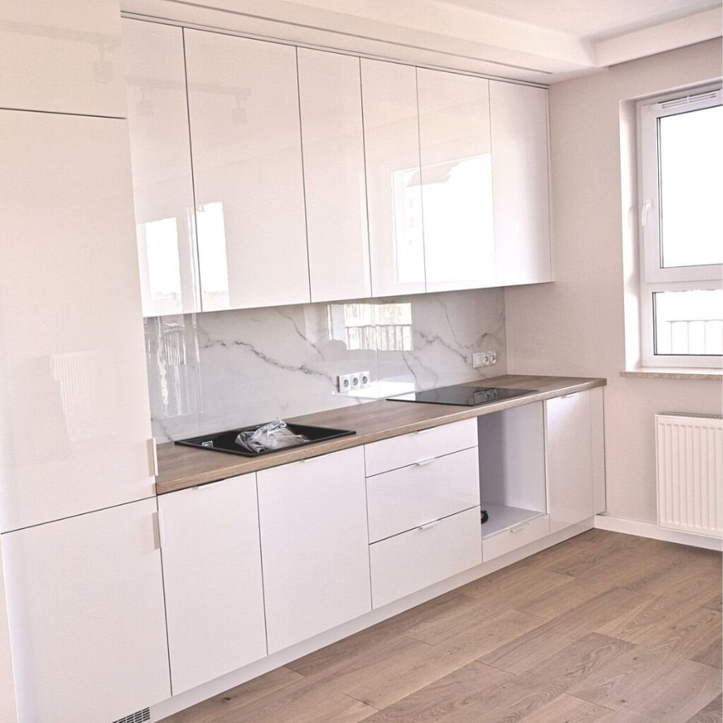 Modern kitchen with glossy white cabinets, light wood countertops, and marble backsplash.